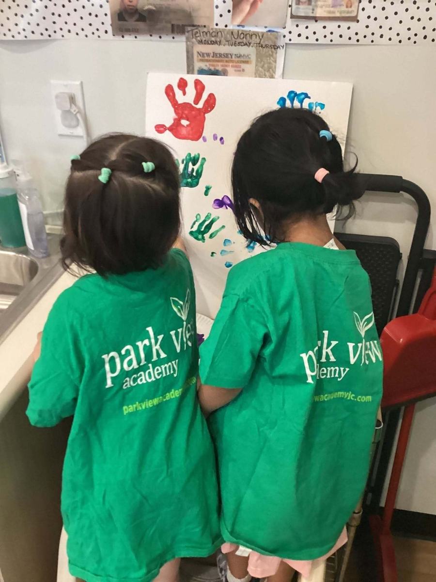 Toddlers in Park View Academy shirts finger-painting at the classroom sink