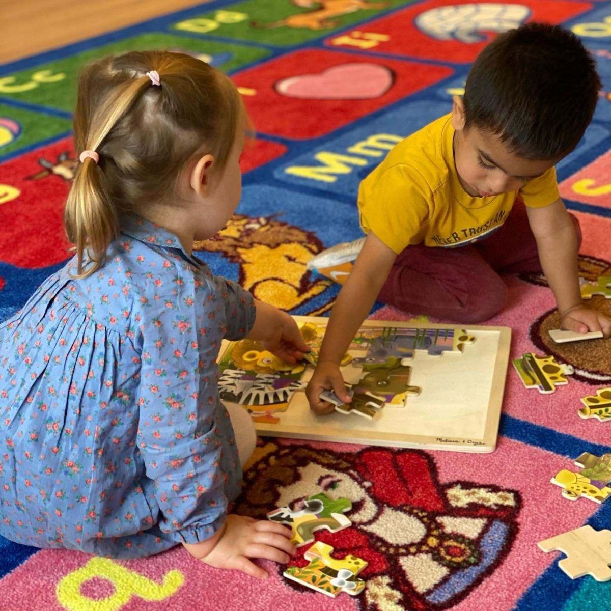 Two children working a wooden puzzle together on the classroom rug at Park View Academy